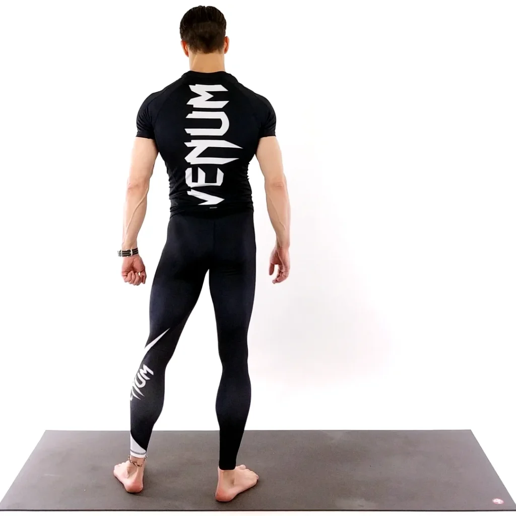 Man in black athletic wear standing on a yoga mat facing away.